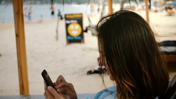 相机在异国度假胜地的躺椅上使用智能手机购物应用程序在快乐的年轻女商人周围移动。