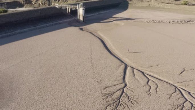 由于气候变化和全球变暖造成的干旱，4k高空中缩小了一个饱受摧残的农民走过干旱大坝的图案化的破裂泥浆表