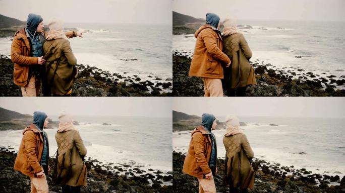在大风天，年轻的幸福夫妇站在海边的岩石上。男人和女人一起探索冰岛。