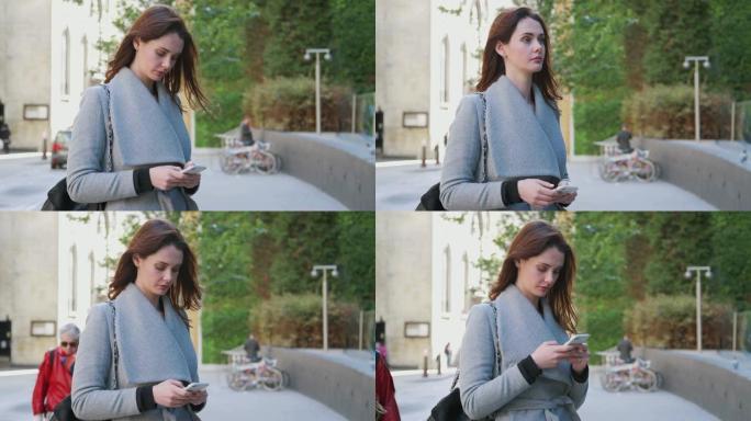 年轻的白人成年妇女站在伦敦的一条街道上，使用智能手机，转身走出镜头特写镜头，专注于前景