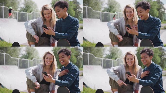 两个女性朋友在城市滑板公园看手机笑