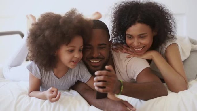 非洲父母与女儿在床上使用有趣的手机应用程序