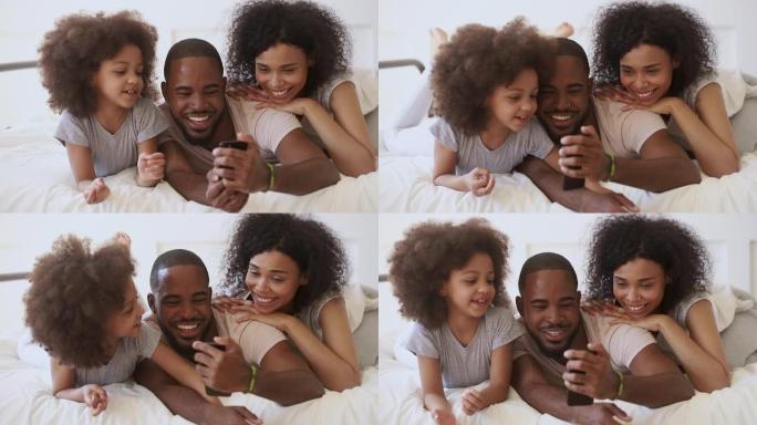 非洲父母与女儿在床上使用有趣的手机应用程序