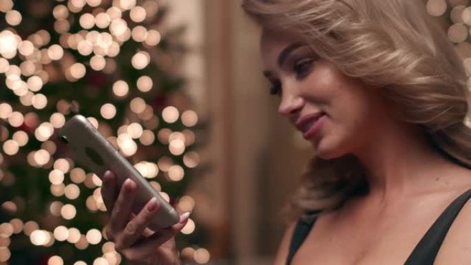 美丽的金发女郎通过电话与她的朋友交流，在美丽的圣诞灯的背景。