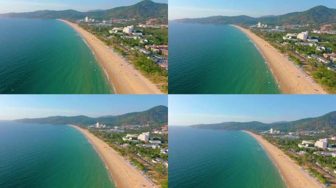 空中4k视图飞越热带蓝色海洋，朝向美丽的绿色山脉和白色沙滩。泰国。普吉岛。卡伦海滩。棕榈滩。岛屿俯视