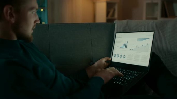 晚上，英俊的年轻人在家放松，躺在客厅的沙发上工作在笔记本电脑上，看着信息图表和统计数据。
