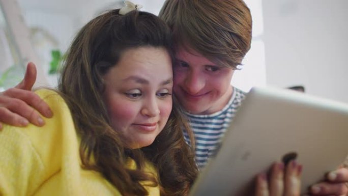 年轻的唐斯综合症夫妇坐在沙发上在家观看数字平板电脑