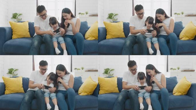 慢动作正常镜头: 快乐温暖的家庭父亲，母亲和女儿在智能手机上在线玩有趣的游戏，一起坐在沙发上，父母带