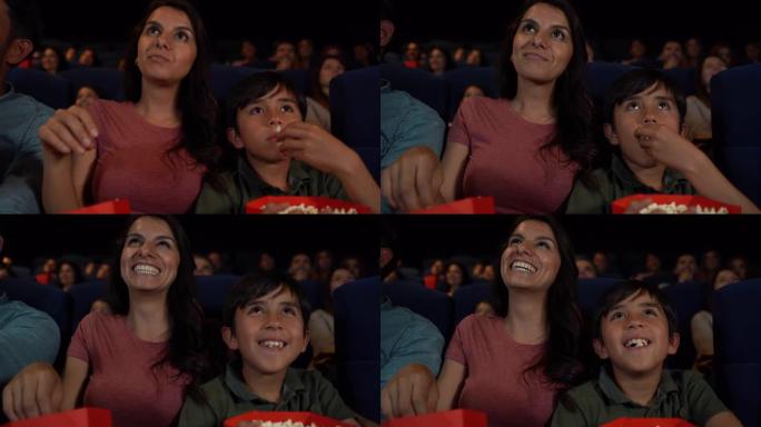妈妈和儿子在电影院欣赏一部有趣的电影，一边笑着吃爆米花