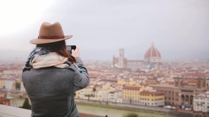 快乐的年轻女性旅行者走上前，拍摄意大利佛罗伦萨秋季惊人城市景观全景的智能手机照片。