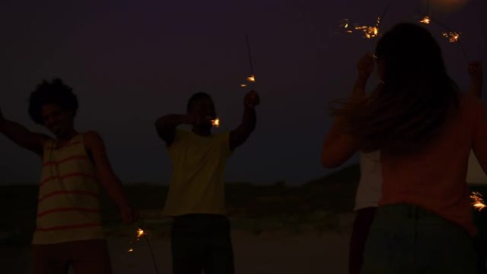 年轻的成年朋友晚上在沙滩上玩火花4k