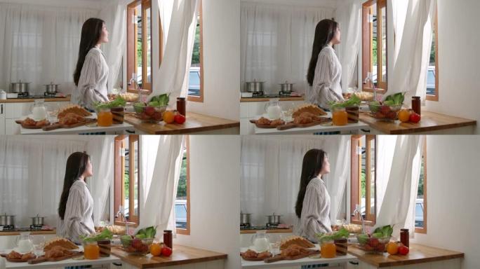 年轻的亚洲迷人的女人在厨房打开窗帘，看着窗户，早上的时候，微笑着，生活方式，自然美丽，感觉在家舒适。
