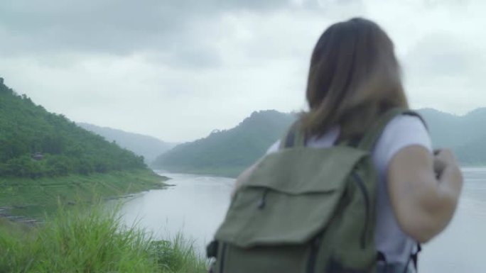 徒步旅行的背包客女人在雨天感受自由行走在湖附近的森林。生活方式女性旅行放松概念。