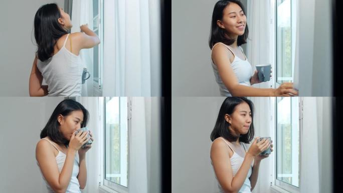 快乐美丽的亚洲女人微笑着在卧室的窗户旁喝一杯咖啡或茶。年轻的拉丁女孩打开窗帘，早上放松。生活方式女人