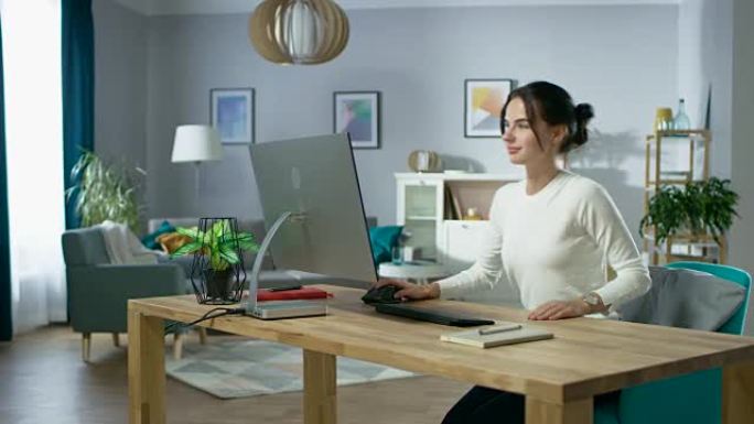 美丽的年轻女孩坐在她的办公桌前，开始在她的个人电脑上工作。背景舒适的生活房间。