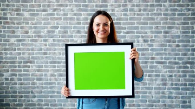 砖墙背景上携带绿色屏幕图片的快乐女孩肖像