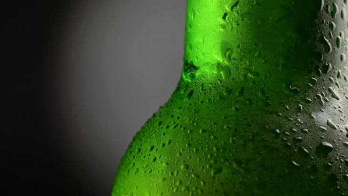 绿色啤酒瓶覆盖着在黑暗背景下旋转的水滴。特写镜头，UHD