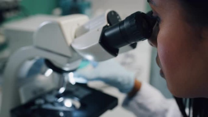 深色皮肤的特写女科学家正在实验室用显微镜分析样本以提取DNA和分子
