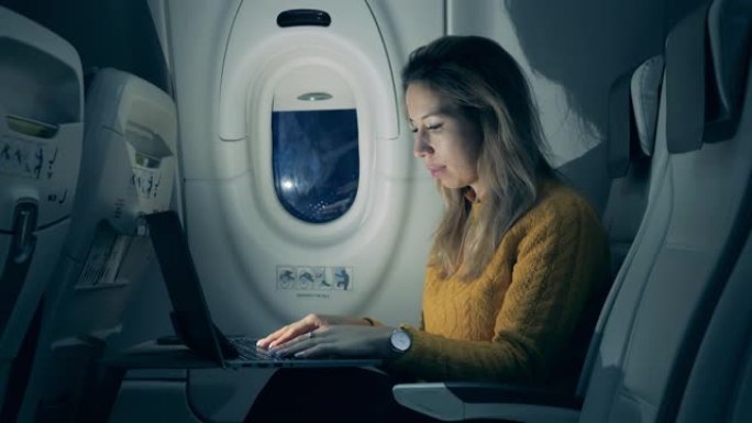 华丽的女人正在飞机机舱里的笔记本电脑上打字。在飞机内工作的女乘客。