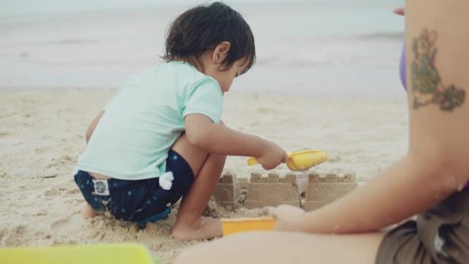 可爱的男婴和年轻的母亲在沙滩上玩沙子。