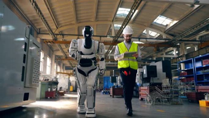 男工程师和一个机器人正沿着工厂行走