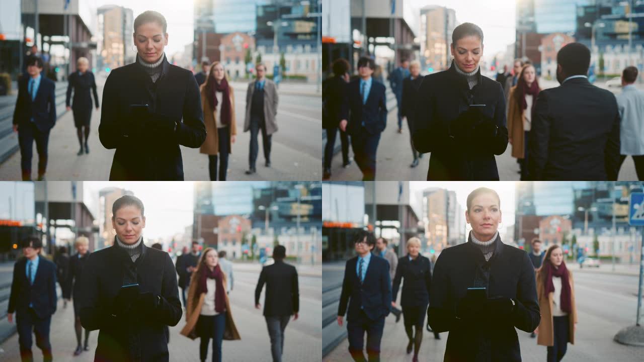 穿着黑色外套的美丽女商人正在市中心的街道上使用智能手机。其他办公室人员走过。她微笑着，看起来很成功。
