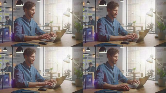 穿着牛仔裤衬衫的英俊创意男性在他阳光明媚的阁楼办公室的笔记本电脑上工作。他看起来很酷，留着胡子。同事