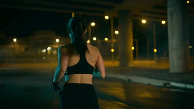 穿着黑色运动上衣和短裤的美丽健身女孩正在街上慢跑。她正在夜间的城市环境中进行锻炼，背景是汽车。