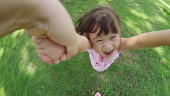 一位母亲在公园里旋转小女儿的镜头，孩子对着镜头微笑