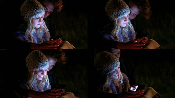 情侣在夜间露营时看手机