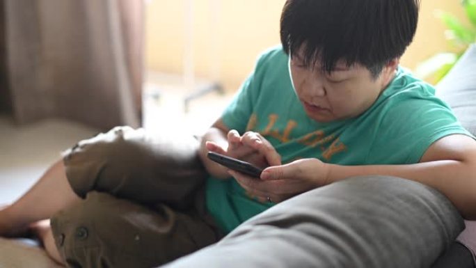 一名亚洲华裔中年妇女下午在客厅的沙发上上网浏览智能手机
