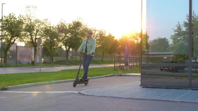 特写: 女人在日出时骑着电动踏板车绕过现代摩天大楼