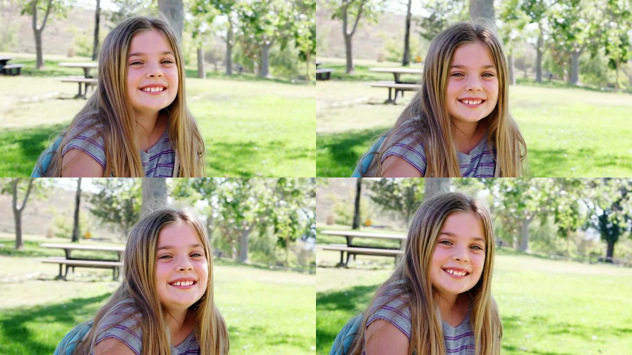 公园里背着背包的年轻女孩的慢动作肖像对着镜头微笑