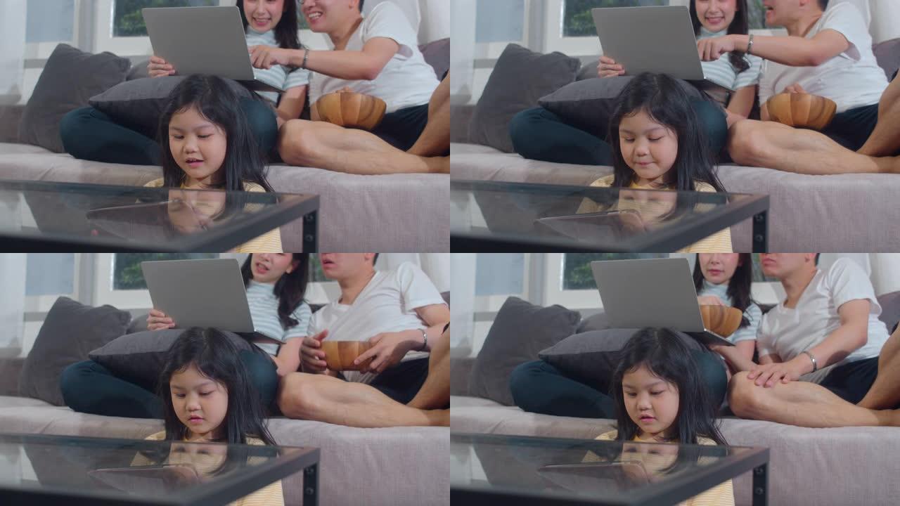 年轻的亚洲家庭和女儿在家里使用平板电脑和笔记本电脑很开心。日本母亲，父亲放松与小女孩看电影，并检查躺