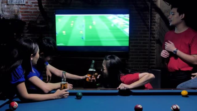 多样化的亚洲朋友在sporstbar观看电视。他们的球队进球并获胜。兴奋的朋友在酒吧喝啤酒时观看足球