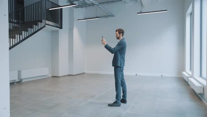 商人站在空荡荡的办公室里，用平板电脑上的增强现实软件来映射它。企业家穿着西装。房间有视频软件的跟踪点