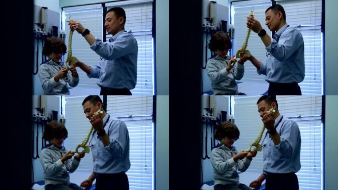 年轻的亚洲男性医生向高加索男孩病人4k展示脊柱模型的侧视图