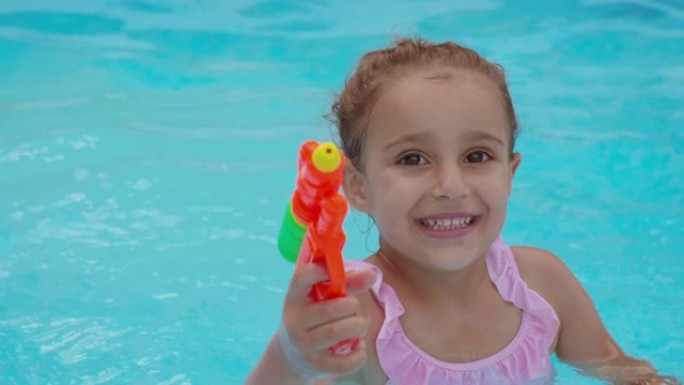 一个快乐的微笑小女孩在游泳池里玩水枪的真实时刻
