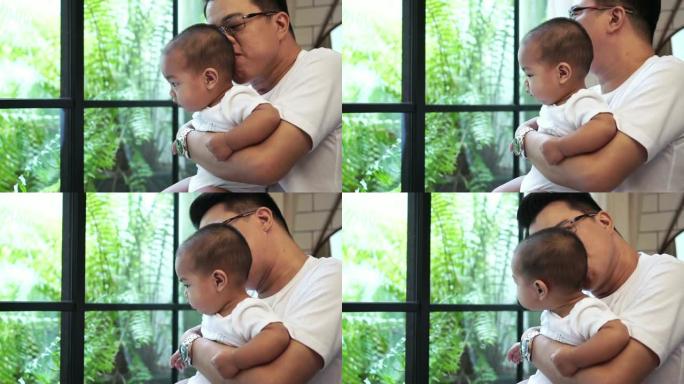 4k慢动作镜头，亚洲男婴凝视着窗户玻璃，而他的父亲则在现代阁楼，家庭和生活方式的概念