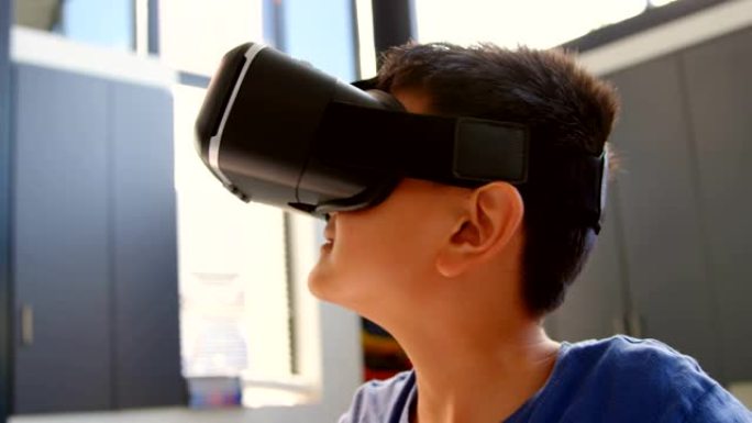 坐在办公桌前并在教室4k中使用虚拟现实耳机的亚洲男生的前视图