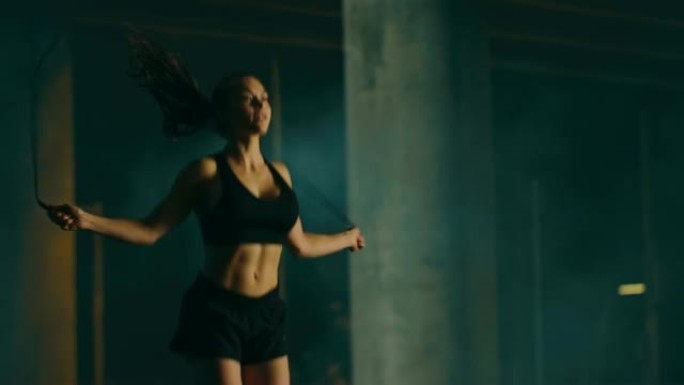 穿着黑色运动上衣和短裤的美丽精力充沛的健身女孩正在跳绳。她正在傍晚雾蒙蒙的城市环境中进行锻炼，背景是