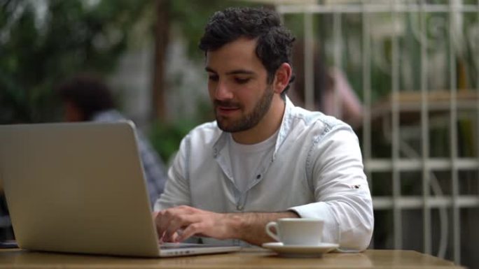 英俊的男人在咖啡店里用笔记本电脑工作，一边喝咖啡，看起来很开心