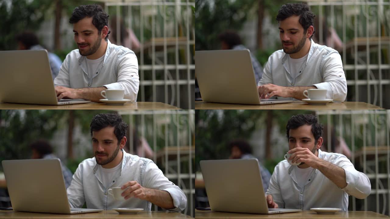 英俊的男人在咖啡店里用笔记本电脑工作，一边喝咖啡，看起来很开心