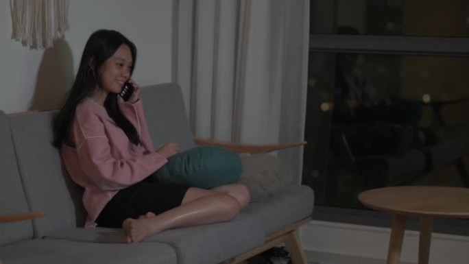 一名亚裔华裔女性晚上在客厅通过电话交谈