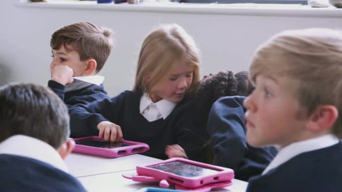 小学生坐在平板电脑教室里的桌子旁，有选择性地集中注意力