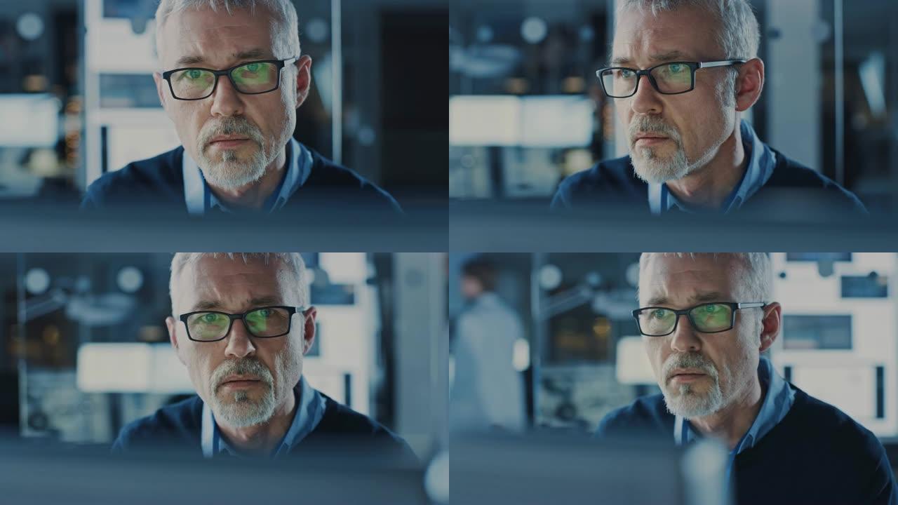 戴着眼镜的英俊中年工程师的肖像在个人电脑上工作。在后台高科技工程设施