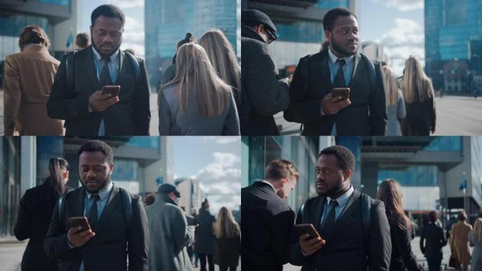 一个穿着西装的非洲裔美国商人的肖像，站在街上，有行人。他在用智能手机。他看起来很成功。其他人去上班。