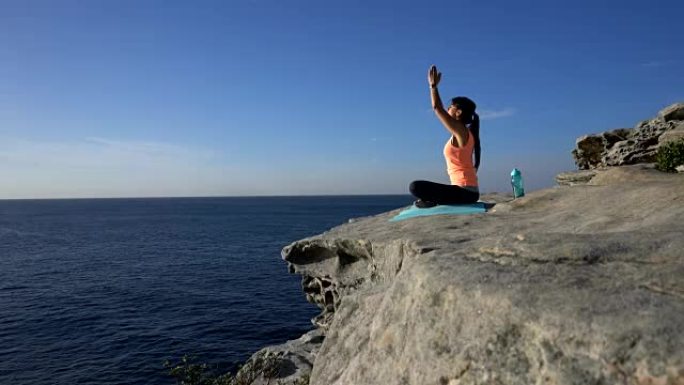 年轻女子坐在海边的悬崖上练习瑜伽