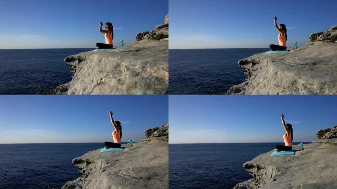 年轻女子坐在海边的悬崖上练习瑜伽