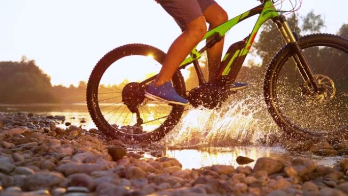 SUN FLARE: 无法识别的运动员在浅溪流中骑山地自行车。